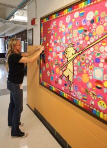 Byam Elementary School art teacher Amy Brown attaches dots created in her class to the bulletin board in the lobby to commemorate International Dot Day on Sept. 15.